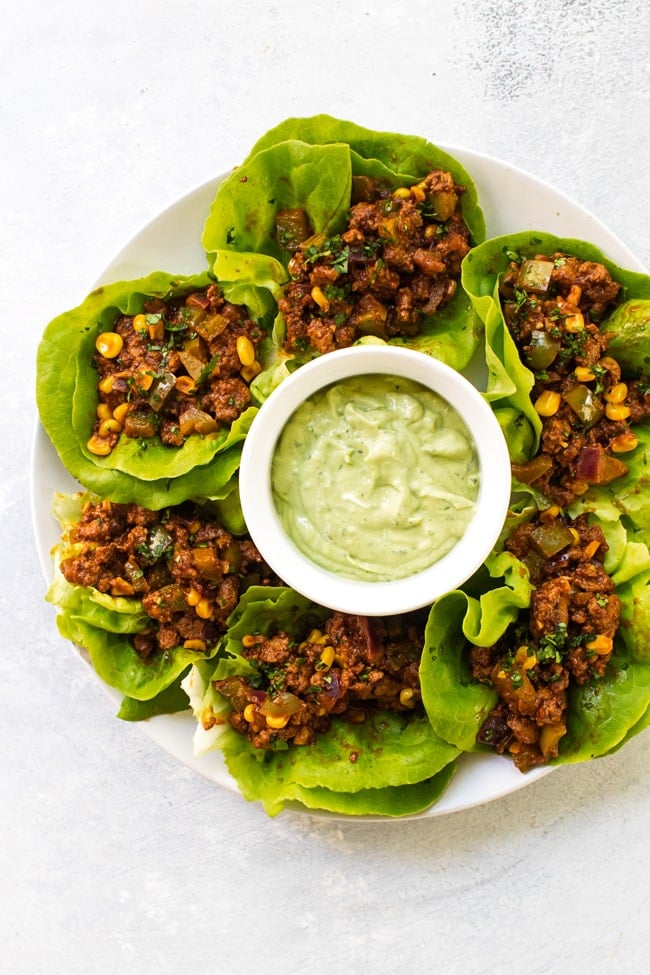 Chipotle beef lettuce wraps on a white plate with a bowl of avocado sauce in the middle