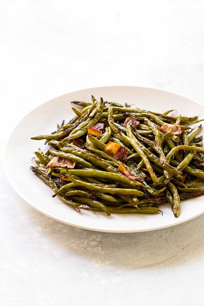 Roasted green beans with bacon tossed with a dill vinaigrette. Served on a white plate.