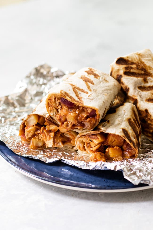 Tropical BBQ chicken wraps sliced in half on some tin foil that is on a blue plate