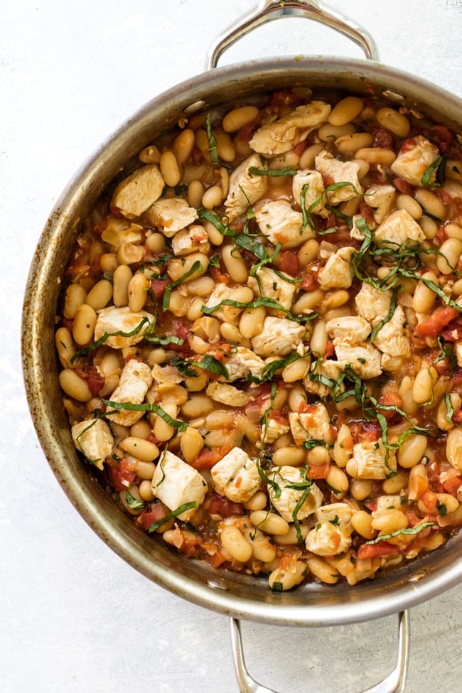 A large skillet with tuscan-style chicken made with white wine, diced tomatoes, white beans and fresh herbs