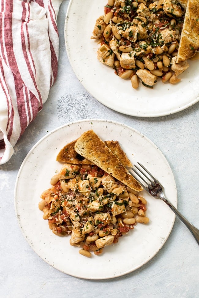 Two servings of tuscan-style chicken skillet on white plates with a red and white striped napkin