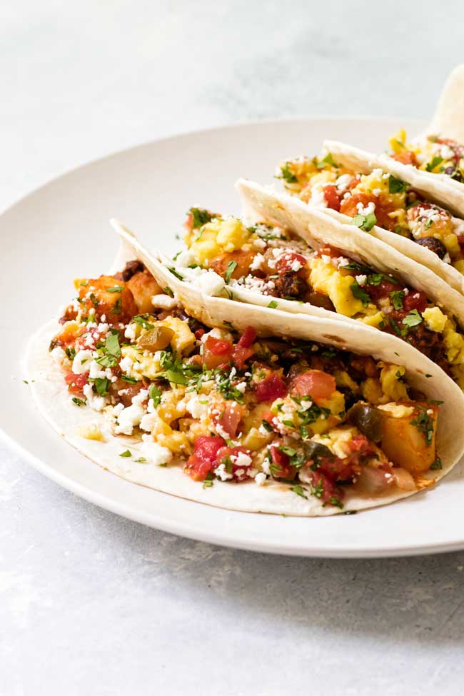 Breakfast tacos topped with cheese and salsa on a white plate