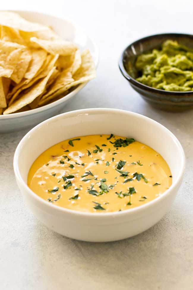 cheese dip in a white bowl with chips and guacamole in the background