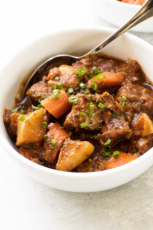 A bowl of slow cooker beef stew with spring vegetables and a spoon