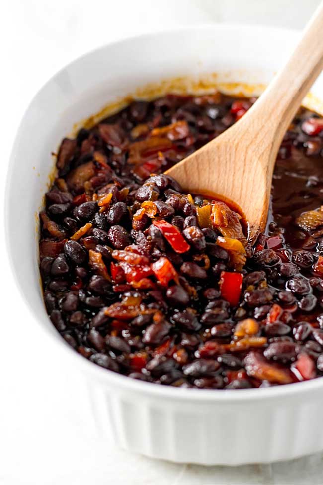 baked black beans in a white dish with a wooden spoon