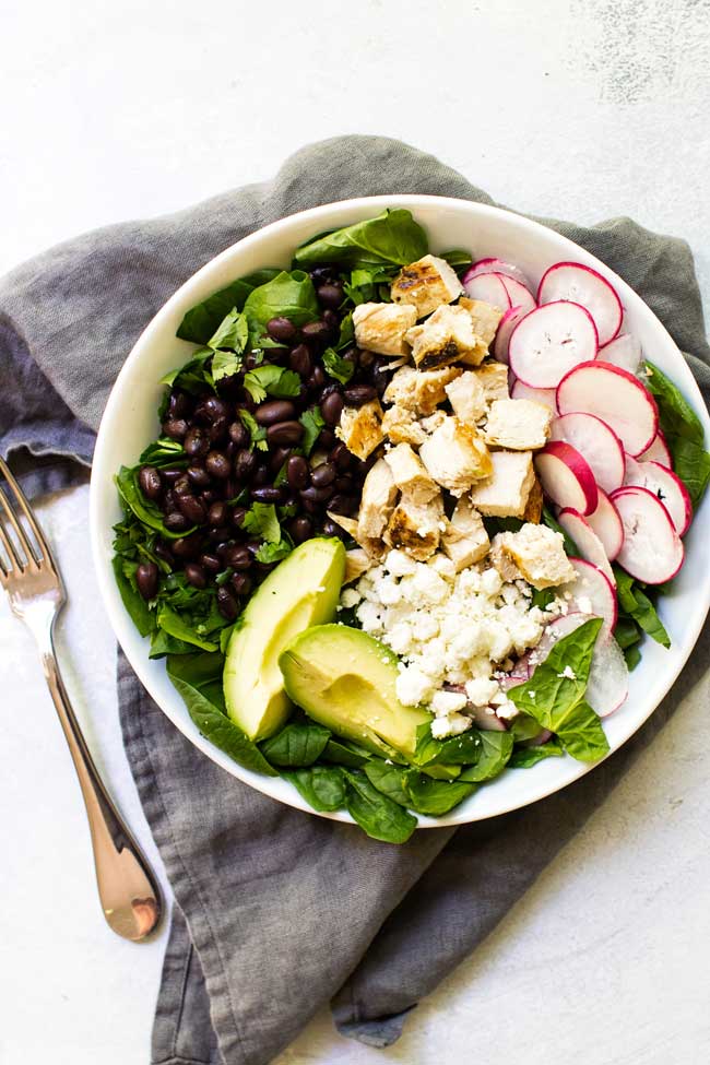 chicken black bean spinach salad in a white bowl with a grey napkin