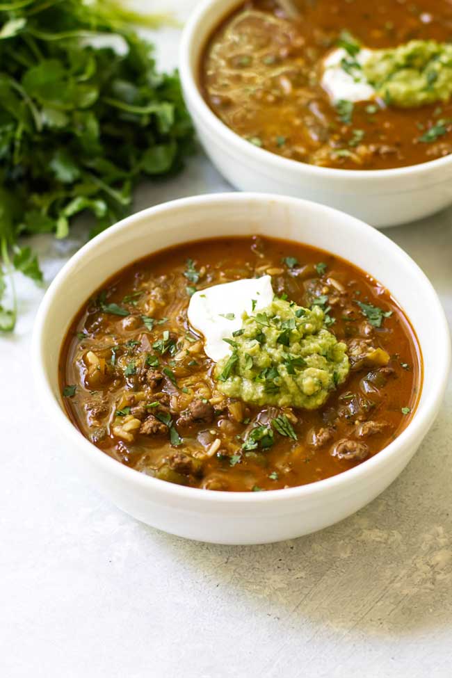 two bowls of salsa verde taco soup garnished with sour cream and guacamole