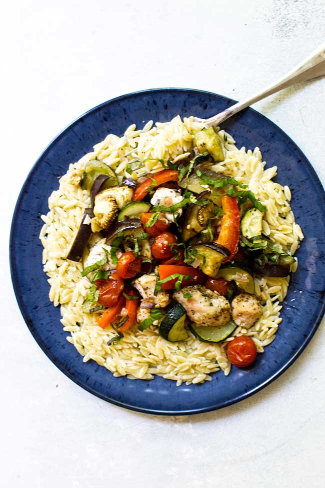 one serving of sheet pan chicken ratatouille on a blue plate with butter herb orzo