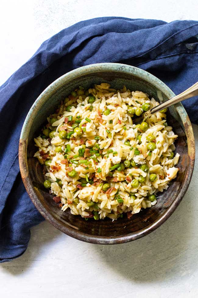 A serving of bacon orzo pasta in a bowl with a fork with a blue napkin