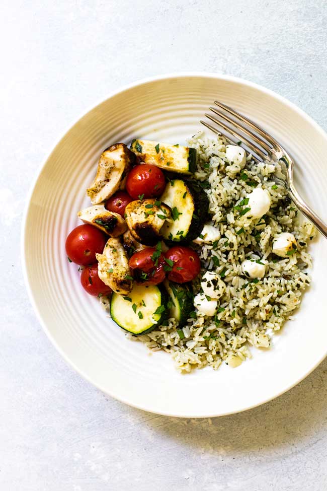 a bowl of chicken, tomatoes, and zucchini with pesto rice