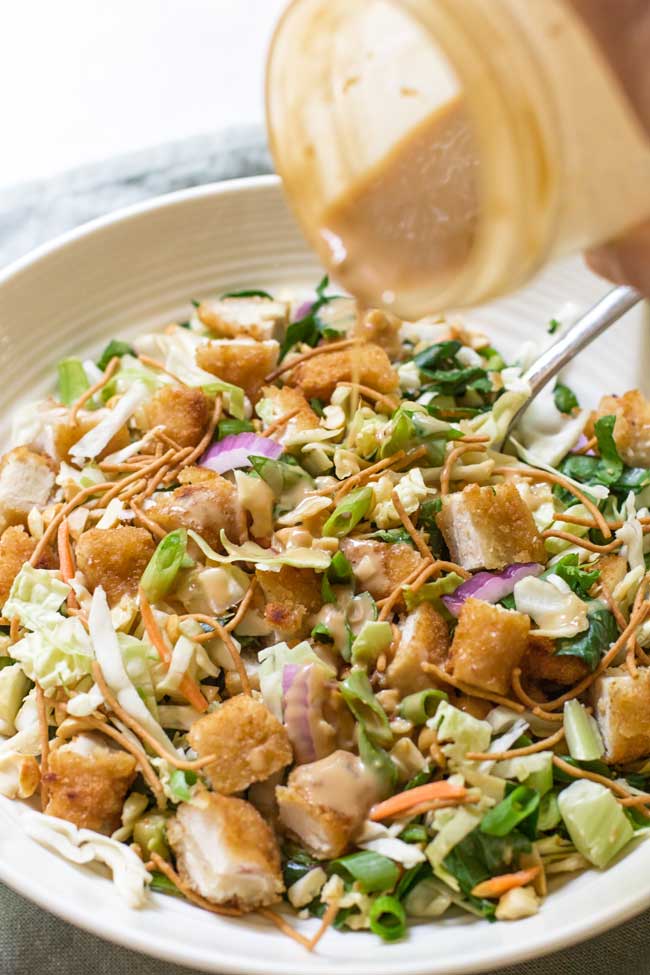 pouring peanut-garlic dressing on the crispy chicken salad