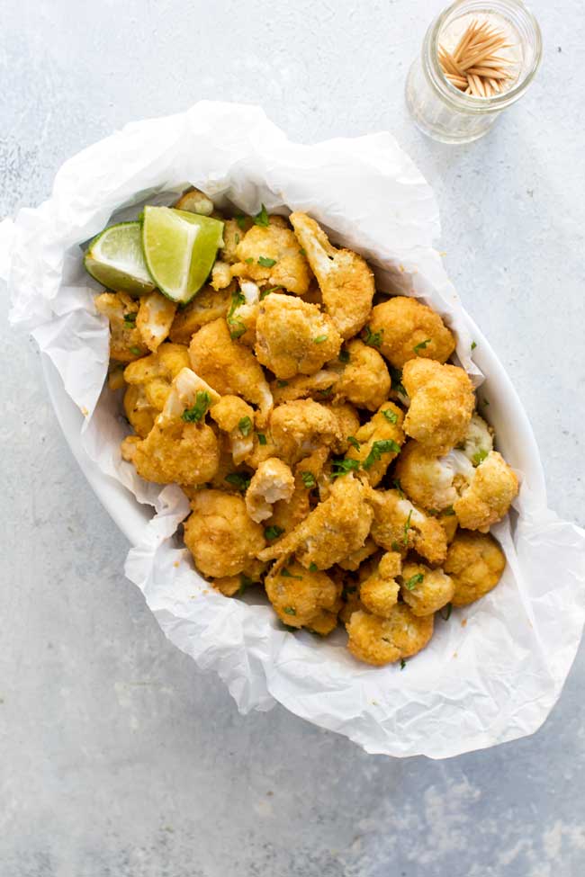 overhead photo of sriracha-lime cauliflower bites in a white dish lined with parchment paper