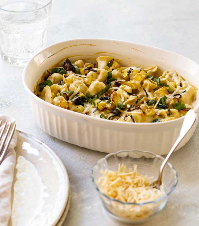 photo of summer squash tortellini bake in a baking dish with a small bowl of grated parmesan cheese