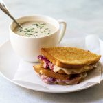 photo of a turkey grilled cheese on a plate with a bowl of cauliflower soup