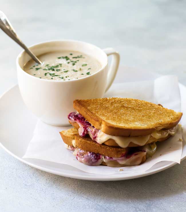 photo of a turkey grilled cheese on a plate with a bowl of cauliflower soup