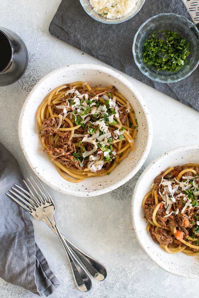 overhead photo of bowls of short rib ragu with a bowl of chopped parsley