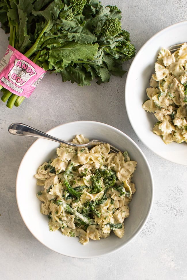 overhead photo of a bowl of broccoli rabe chicken pasta with a bunch of fresh broccoli rabe