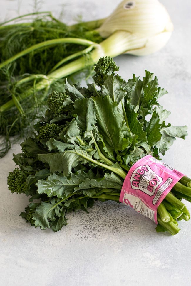 Photo of a bunch of Andy Boy broccoli rabe with a bulb of fennel in the background