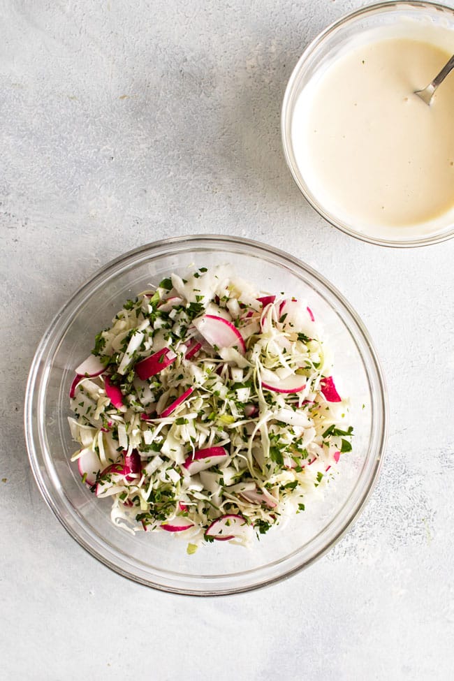 overhead photo of a bowl of chopped cabbage, radishes, and jicama and a small bowl of dressing