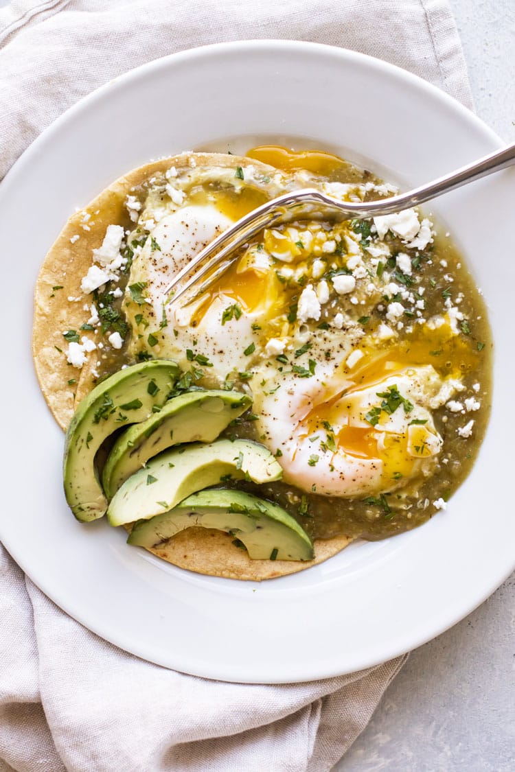 overhead photo of salsa verde eggs on corn tortillas with avocado and feta