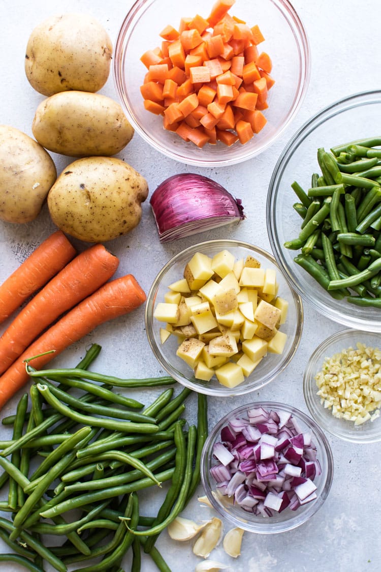 overhead photo of potatoes, carrots, onions, green beans chopped in bowls and whole