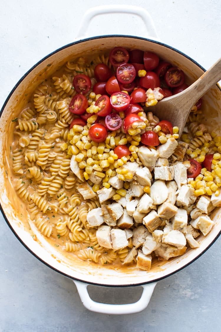 overhead photo of corn, chicken and tomatoes being stirred into the pasta and sauce