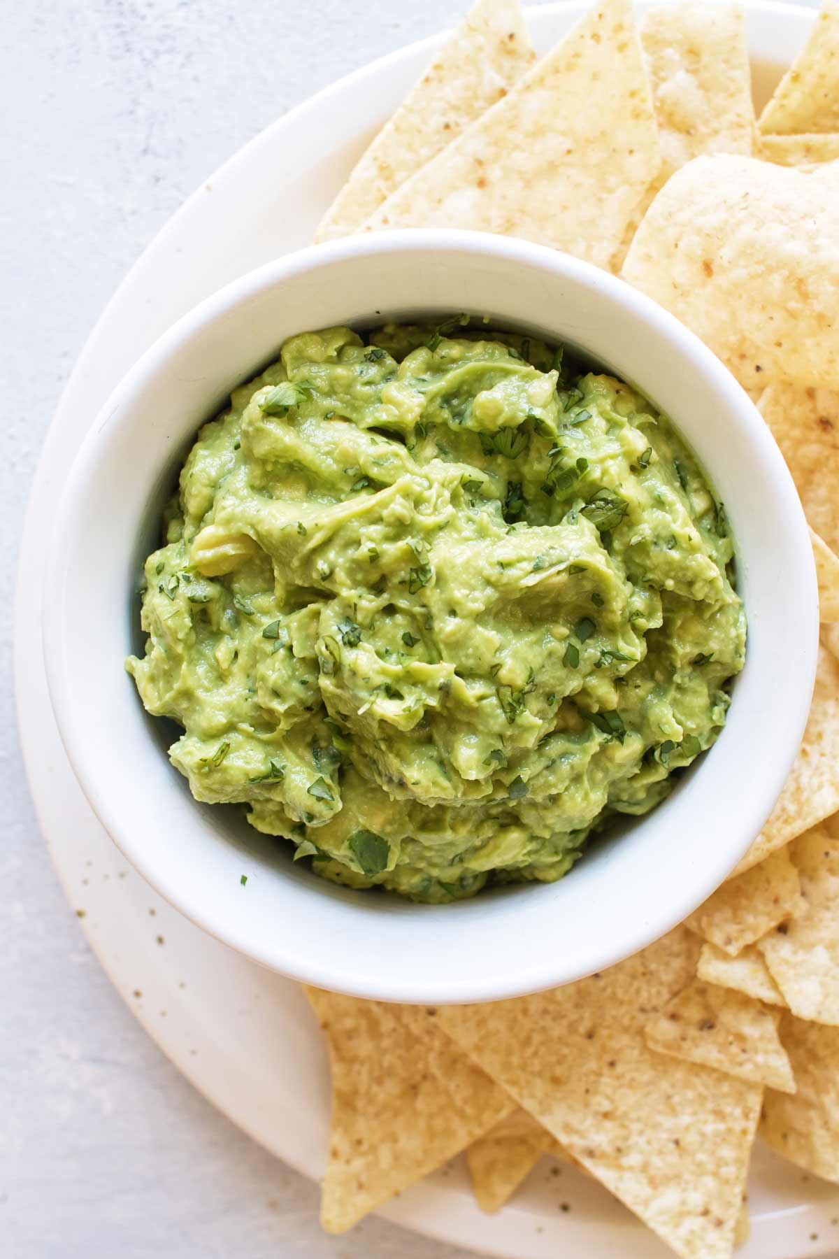 overhead photo of a bowl of guacamole on a plate with chips