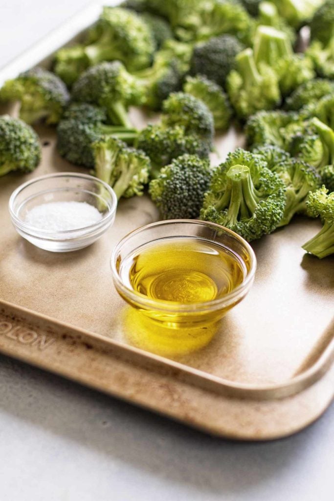 photo of a small bowl of oil and salt on a baking sheet with raw broccoli