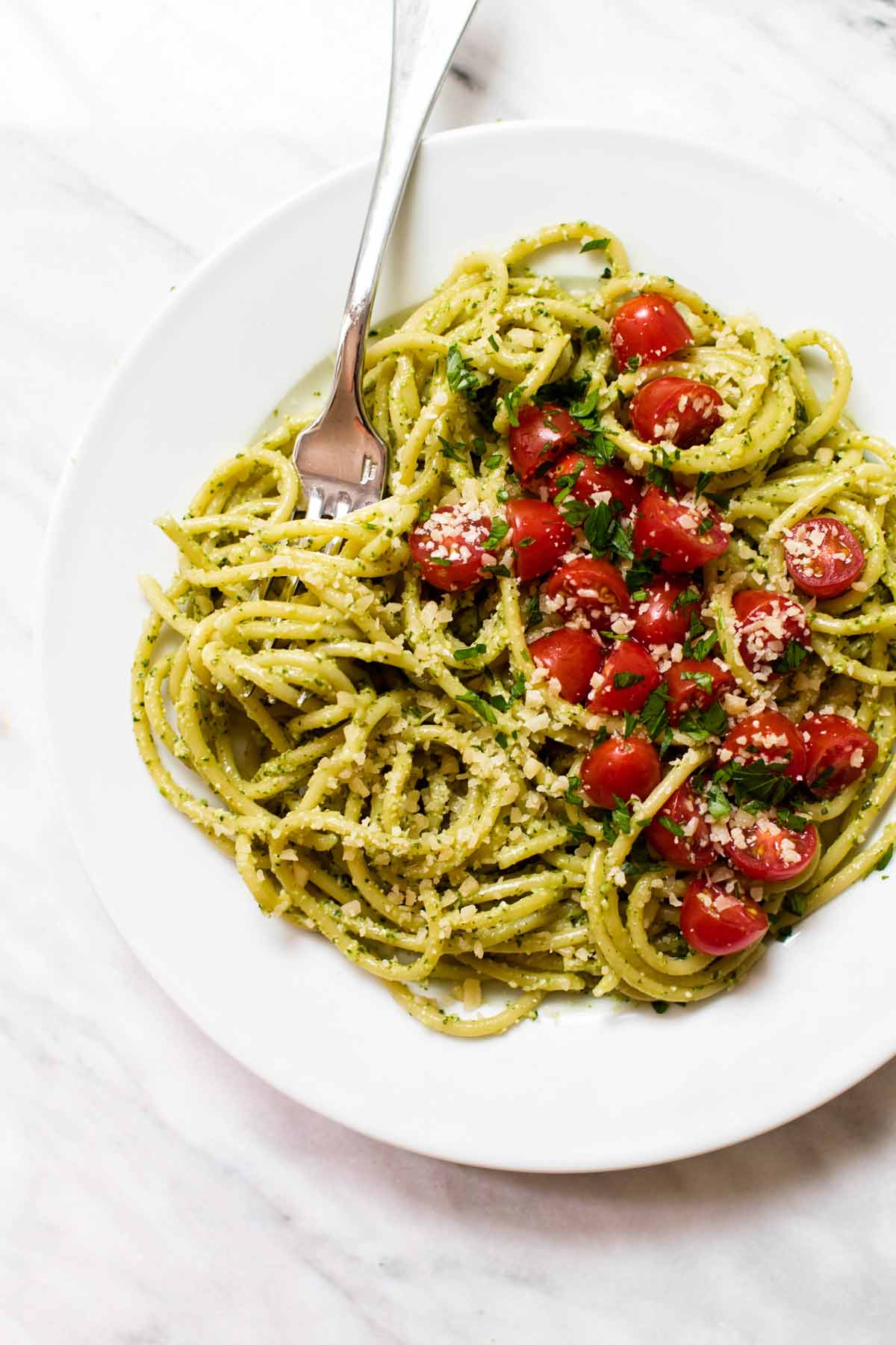 overhead photo of a plate of pasta with pesto and fresh tomatoes