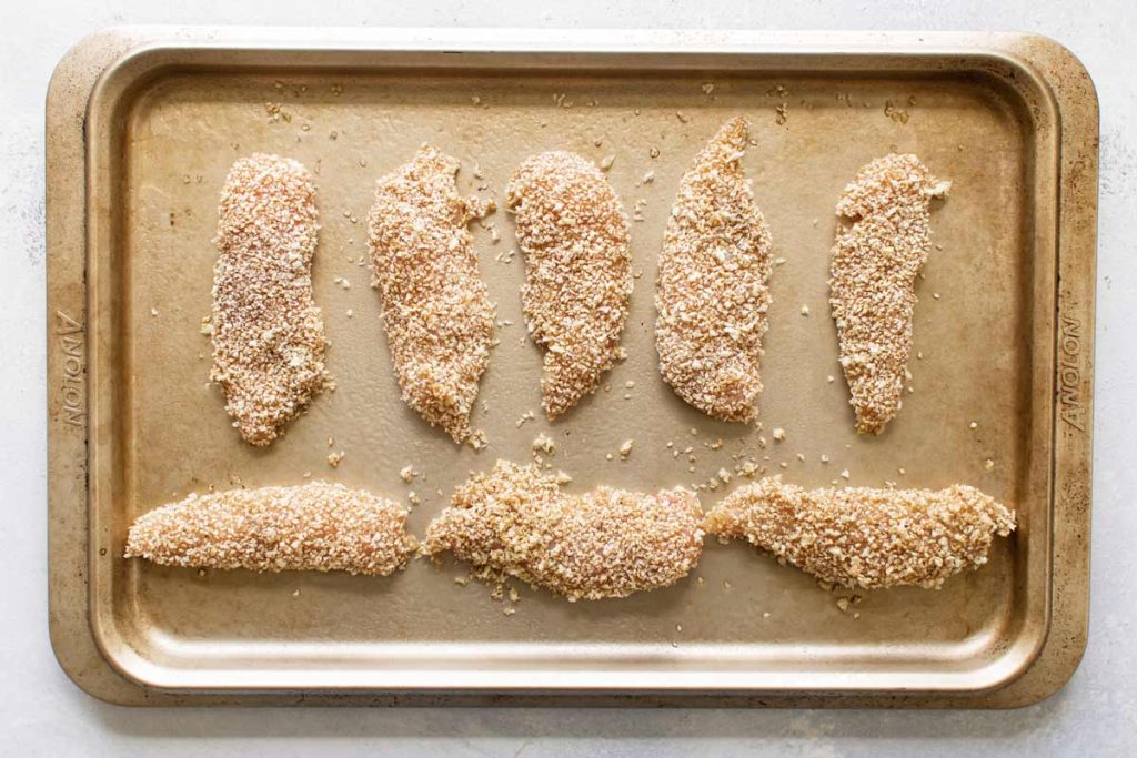 overhead photo of the chicken breaded with sesame seeds and panko on a baking sheet