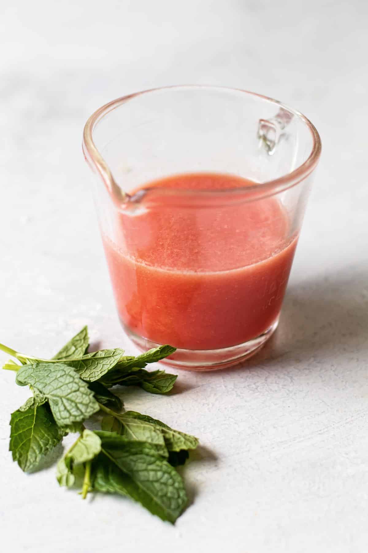 photo of fresh mint and a small measuring cup with watermelon juice