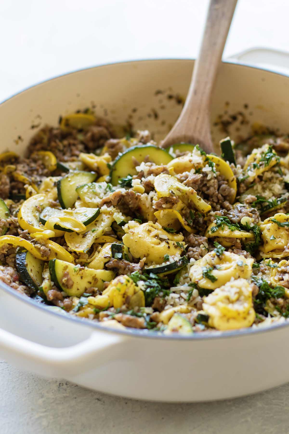 a pan of pesto tortellini with a wooden spoon.