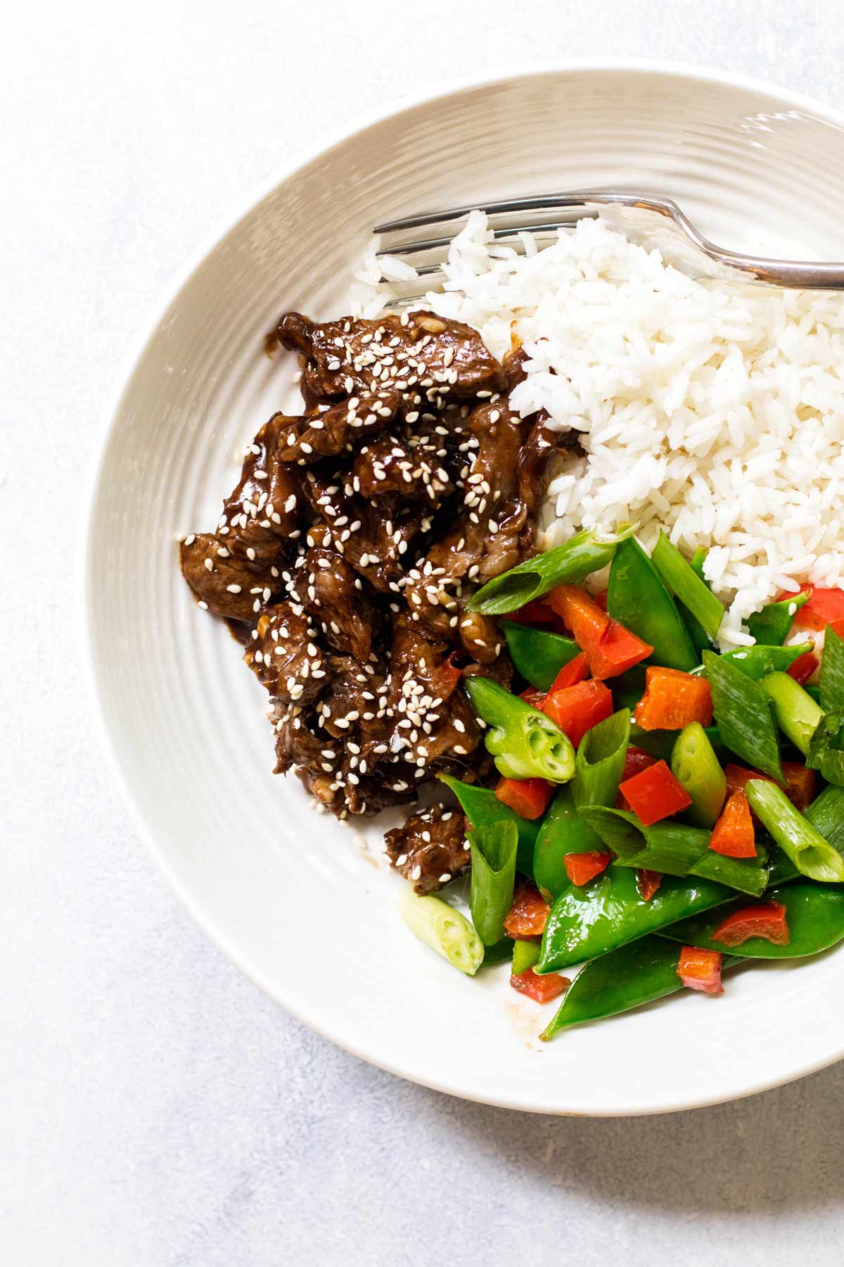 photo of a a bowl of sesame beef with rice and veggies.