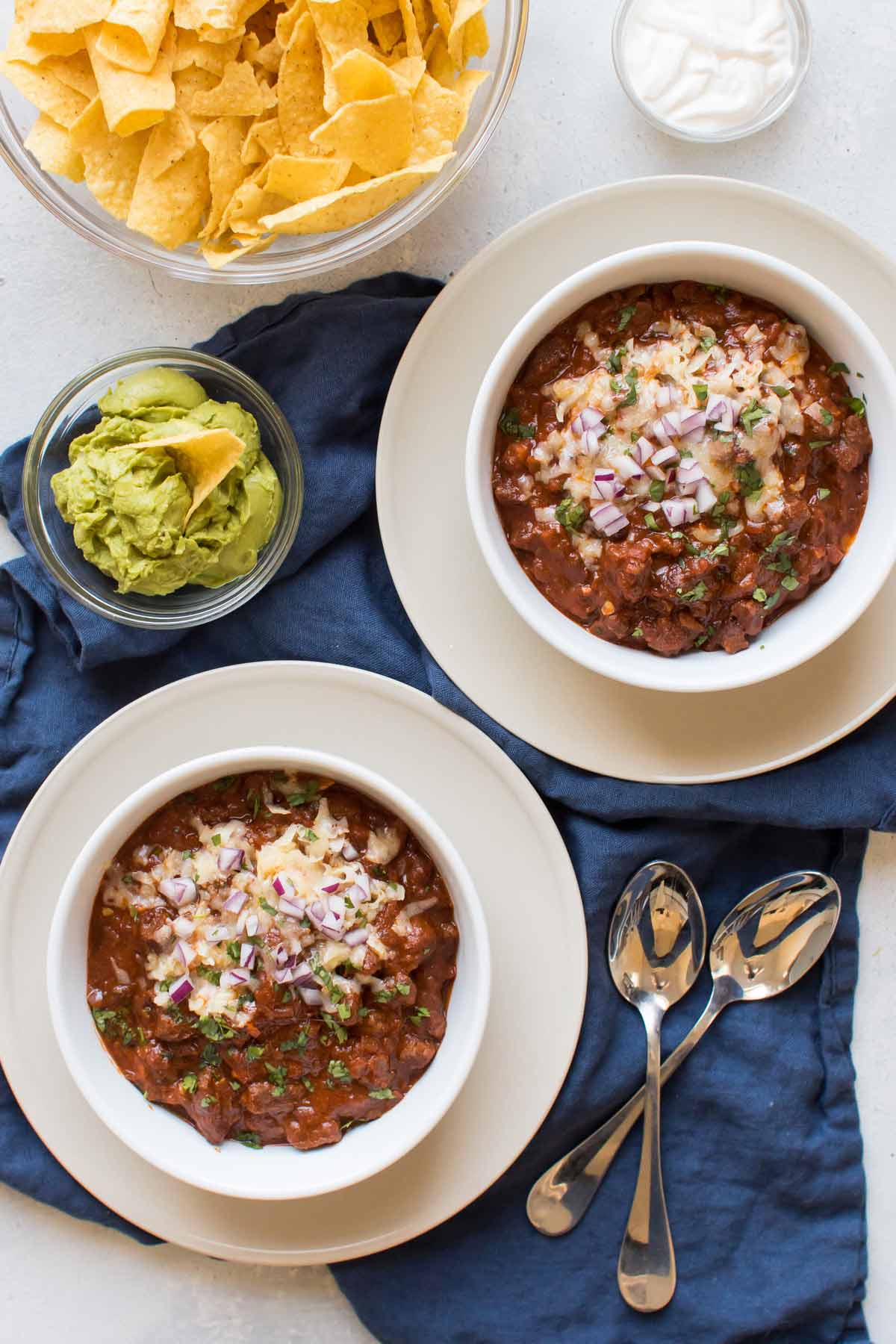 overhead shot of two bowls of chili with tortilla chips, sour cream, and tortilla chips on the side.