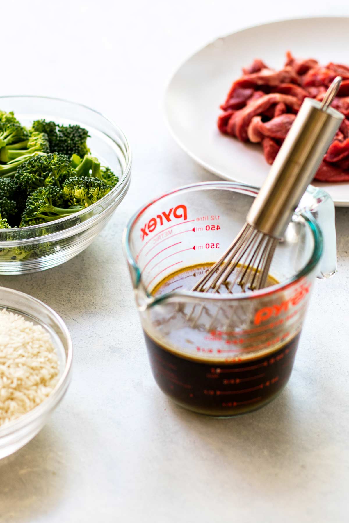 sauce in a measuring cup with broccoli and meat in the background