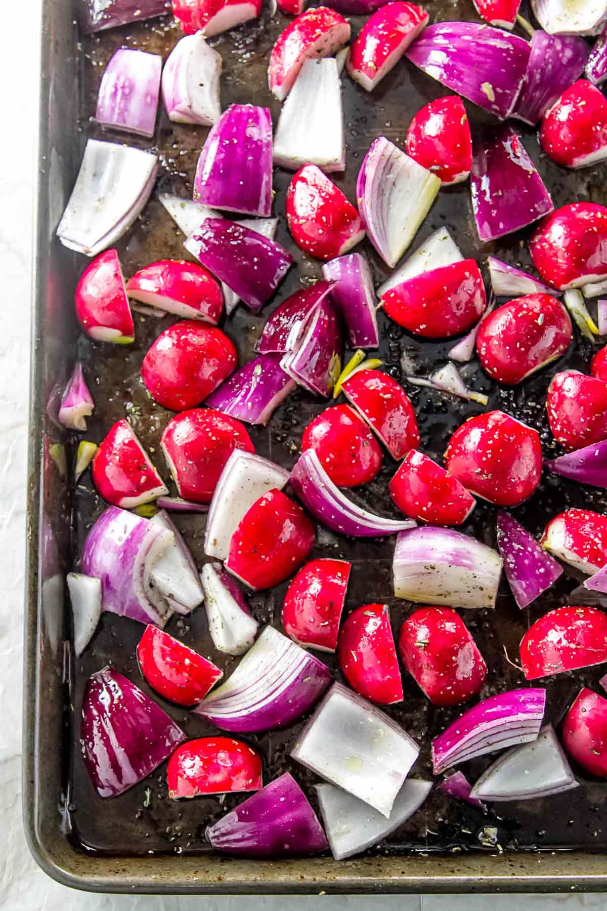 radishes and onion on a sheet pan ready to be roasted.