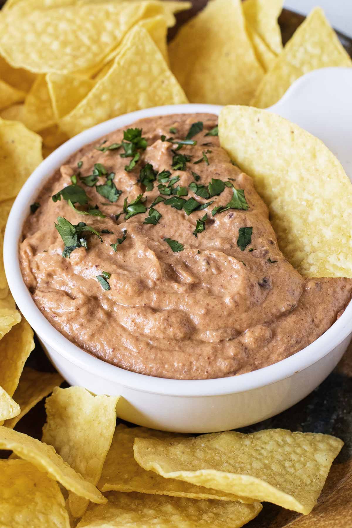 a bowl of bean dip on a platter with tortilla chips.