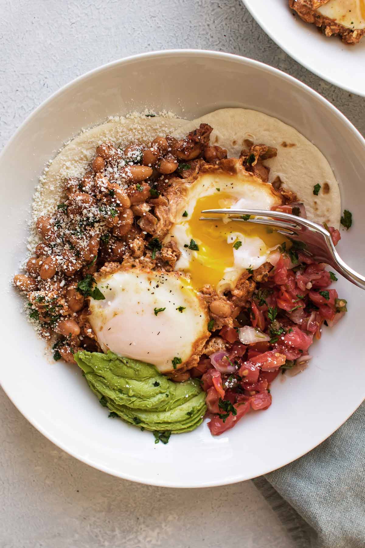 overhead photo of a bowl of ranch eggs with a fork breaking the yolk.