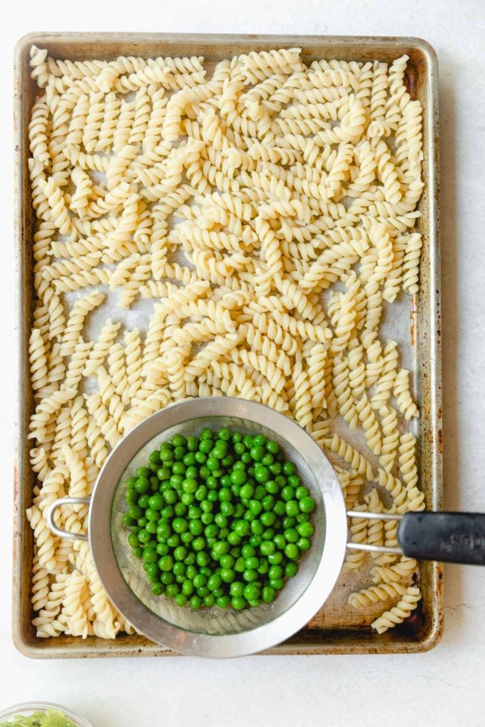 cooked pasta on a sheet pan with thawed peas.