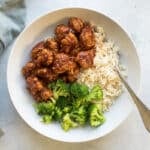 orange chicken in a bowl with rice and broccoli.