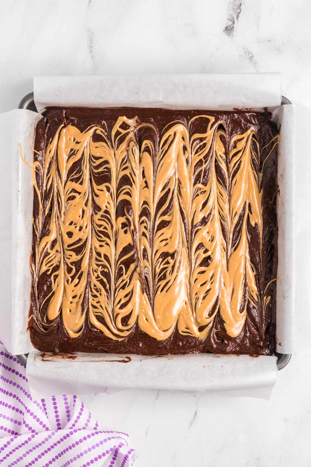 brownie batter in pan with peanut butter swirled on top.