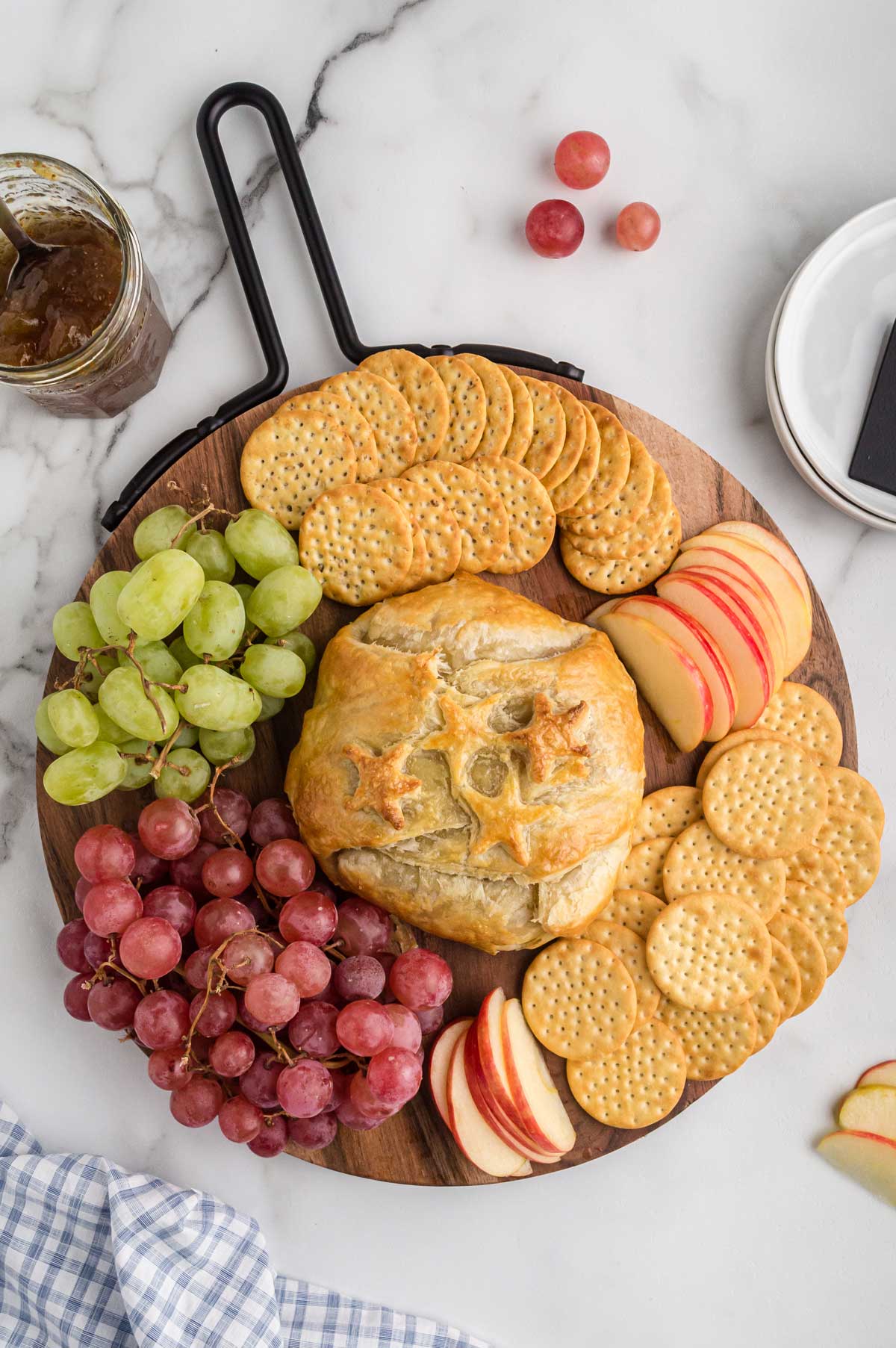 baked brie on a platter with grapes, apples, and crackers.