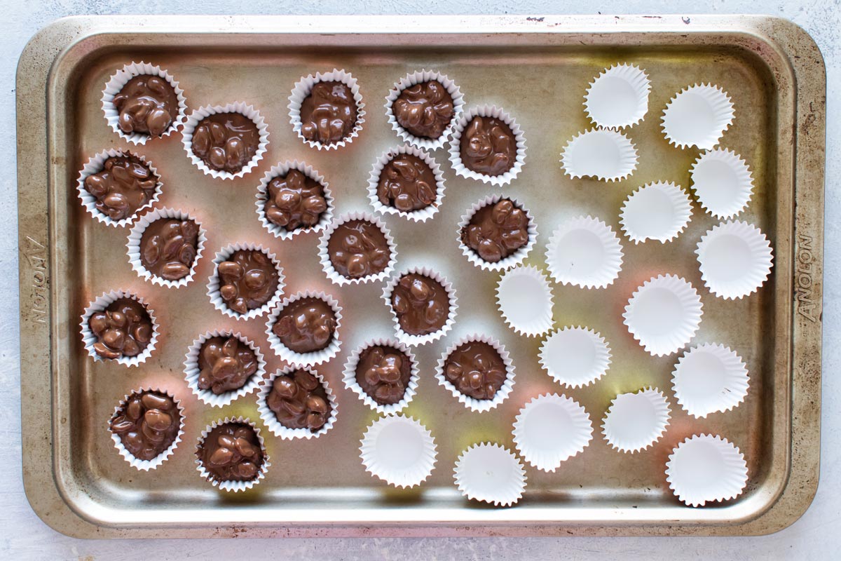 overhead shot of mini paper liners being filled with the melted chocolate and nuts.