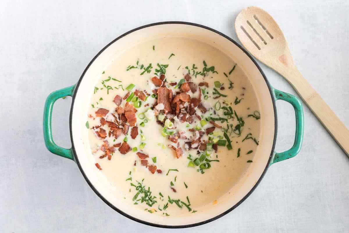potato soup in a pot garnished with bacon and green onions.