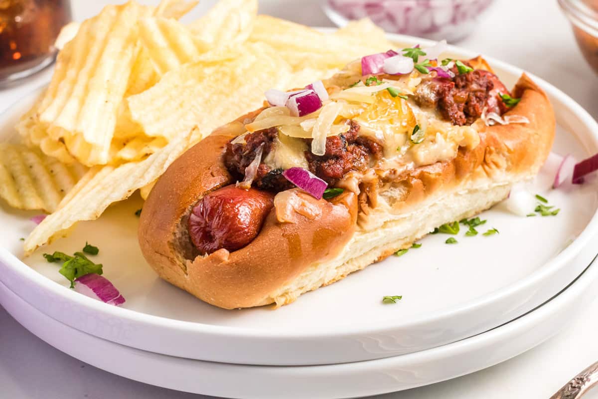 a chili cheese dog on a plate with chips.