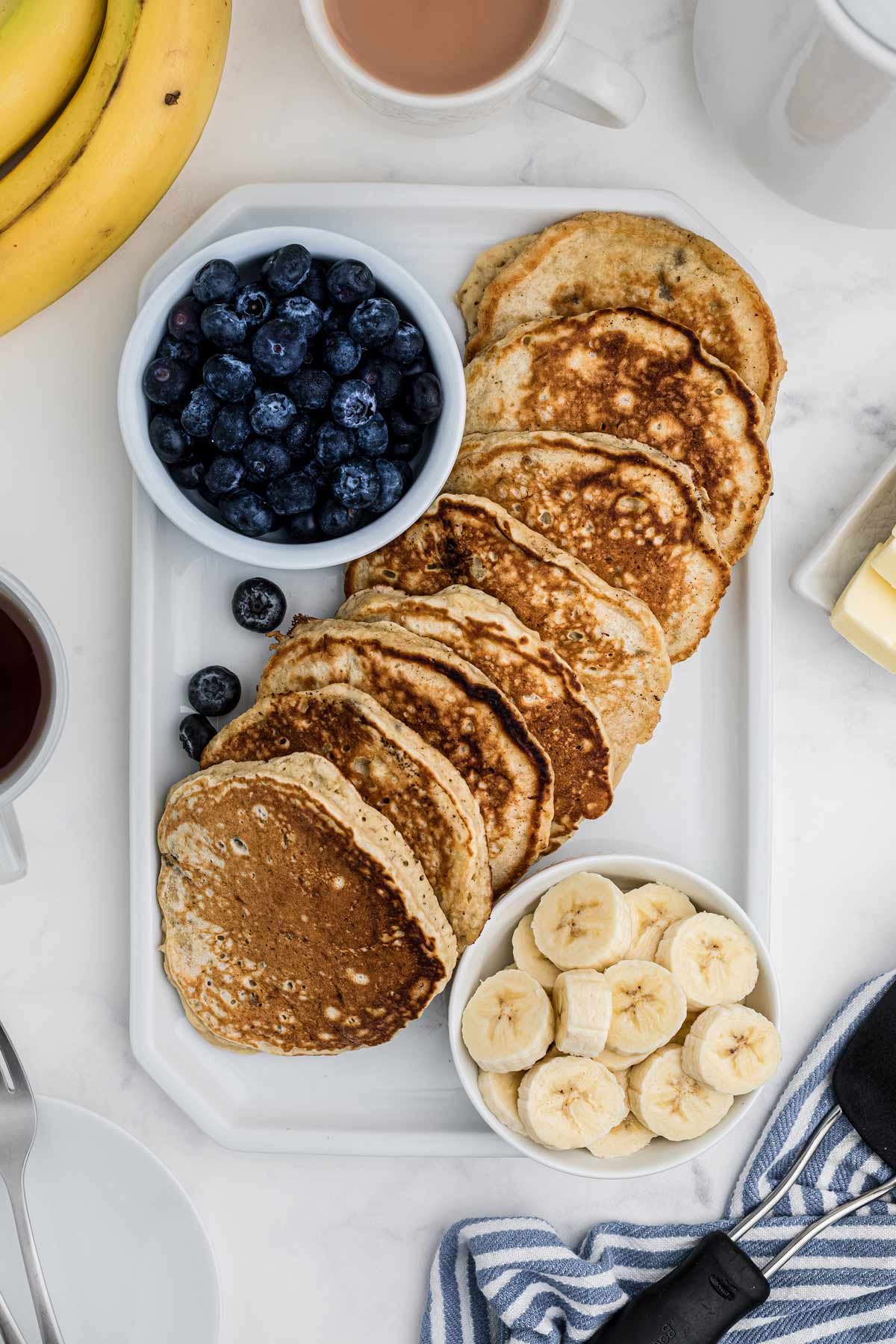 overhead shot of the pancakes on a plate with a bowl of blueberries and bananas.