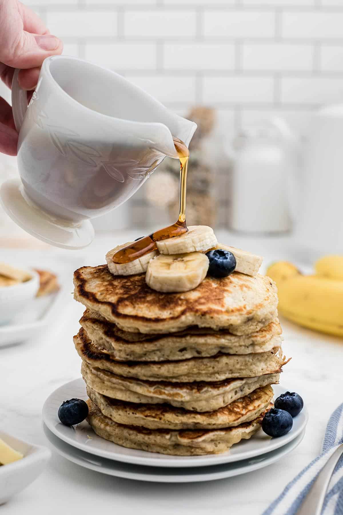 syrup being poured over a stack of pancakes.