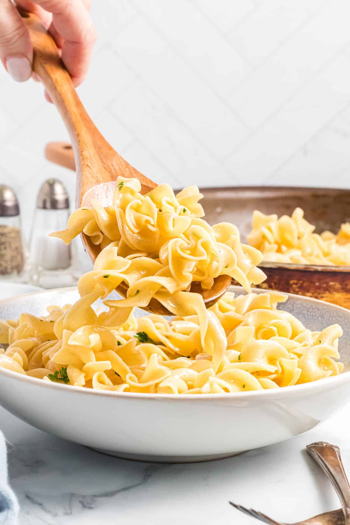 buttered noodles being spooned into a serving bowl.