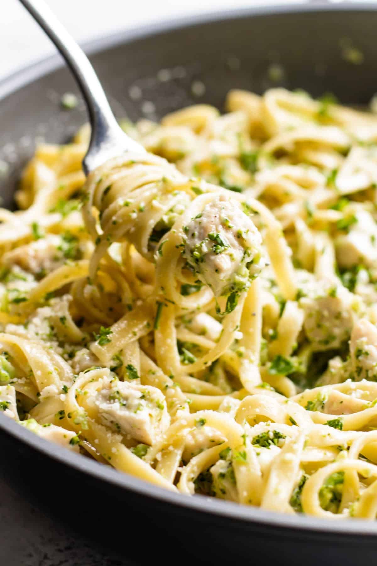 a forkful of broccoli chicken alfredo being lifted out of a pan.