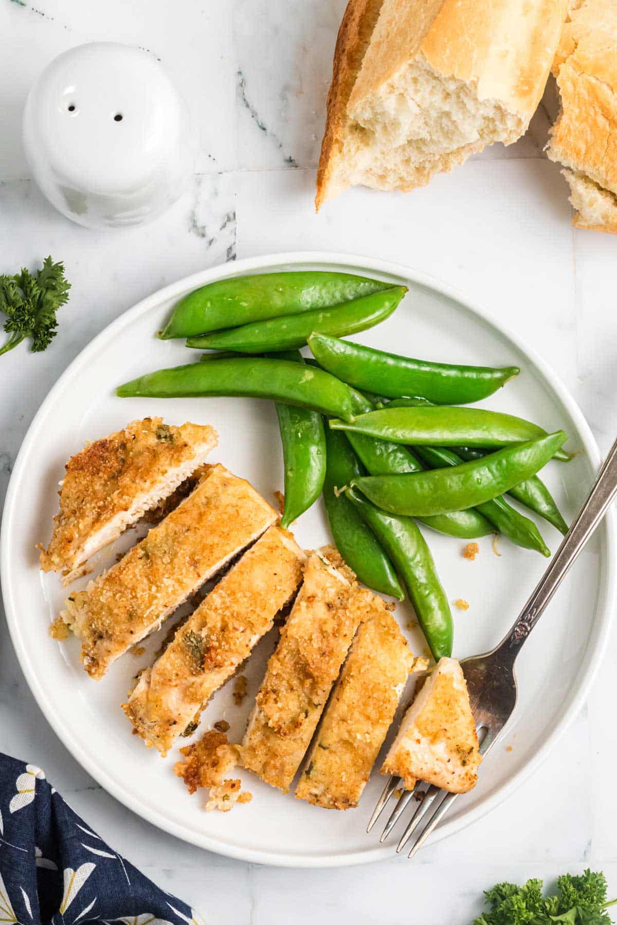 overhead shot of sliced baked breaded chicken on a plate with snap peas.